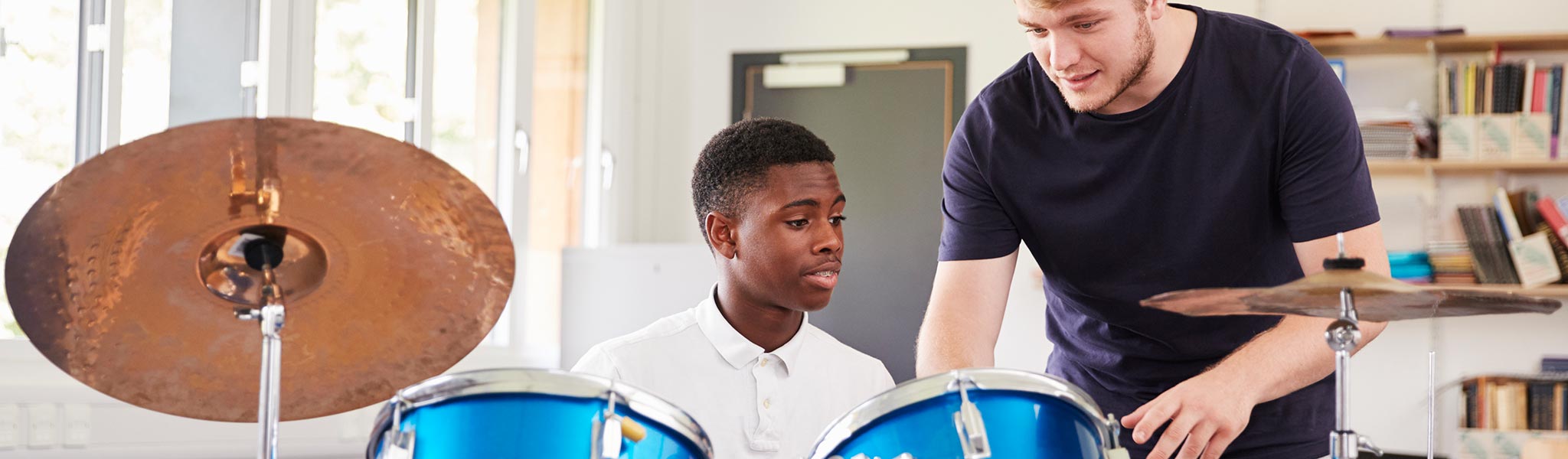 Male Pupil With Teacher Playing Drums In Music Lesson Male Pupil With Teacher Playing Drums In Music Lessonq